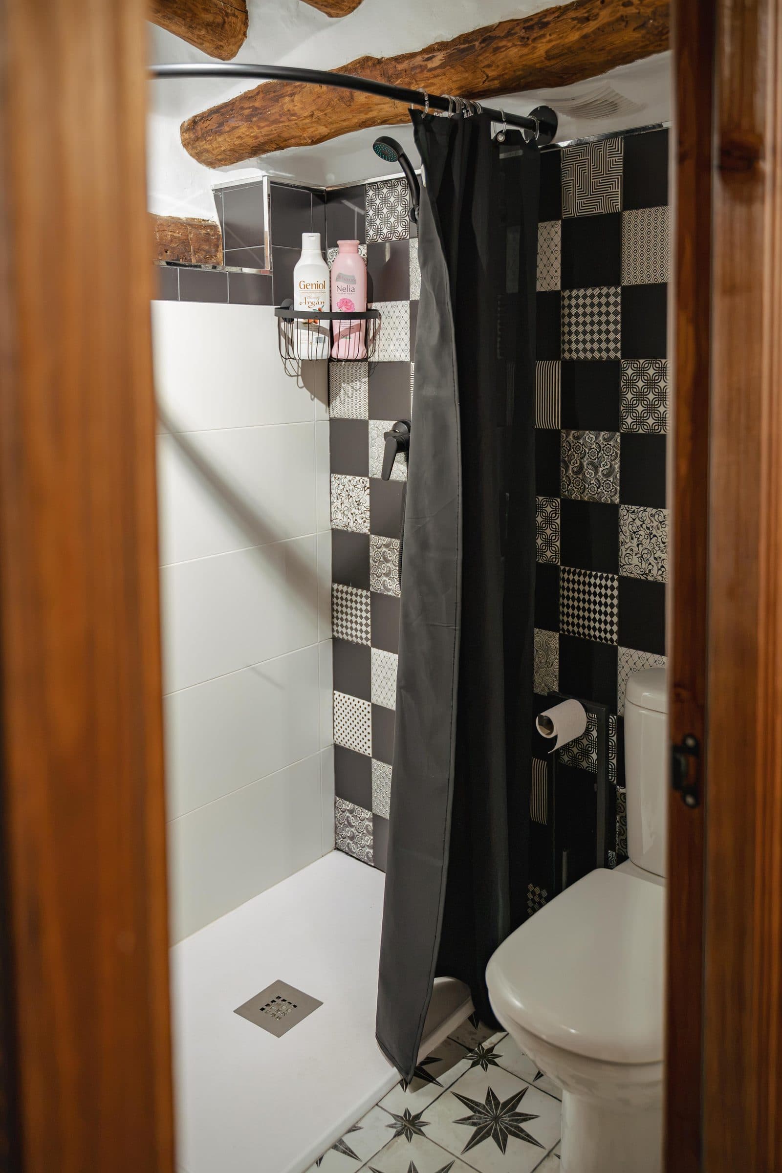 Baño con ducha y alicatado en damero bajo las vigas de madera, en Casa Cuadra, en Albondón