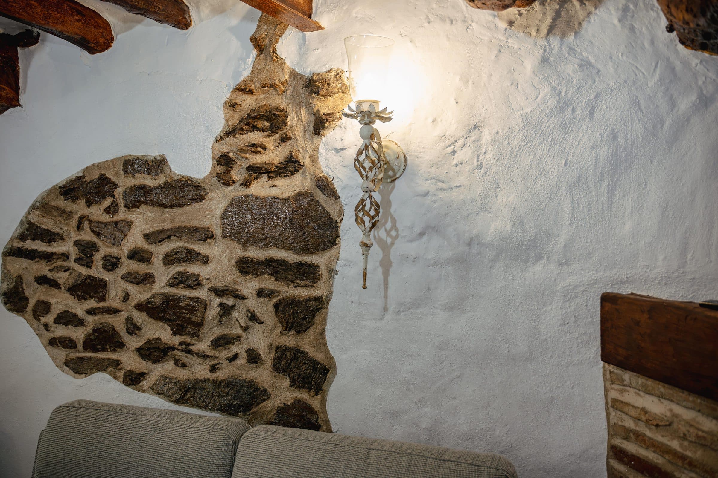 Pared de cal y piedra con lámpara de forja y vigas de madera, en Casa Cuadra, en Albondón