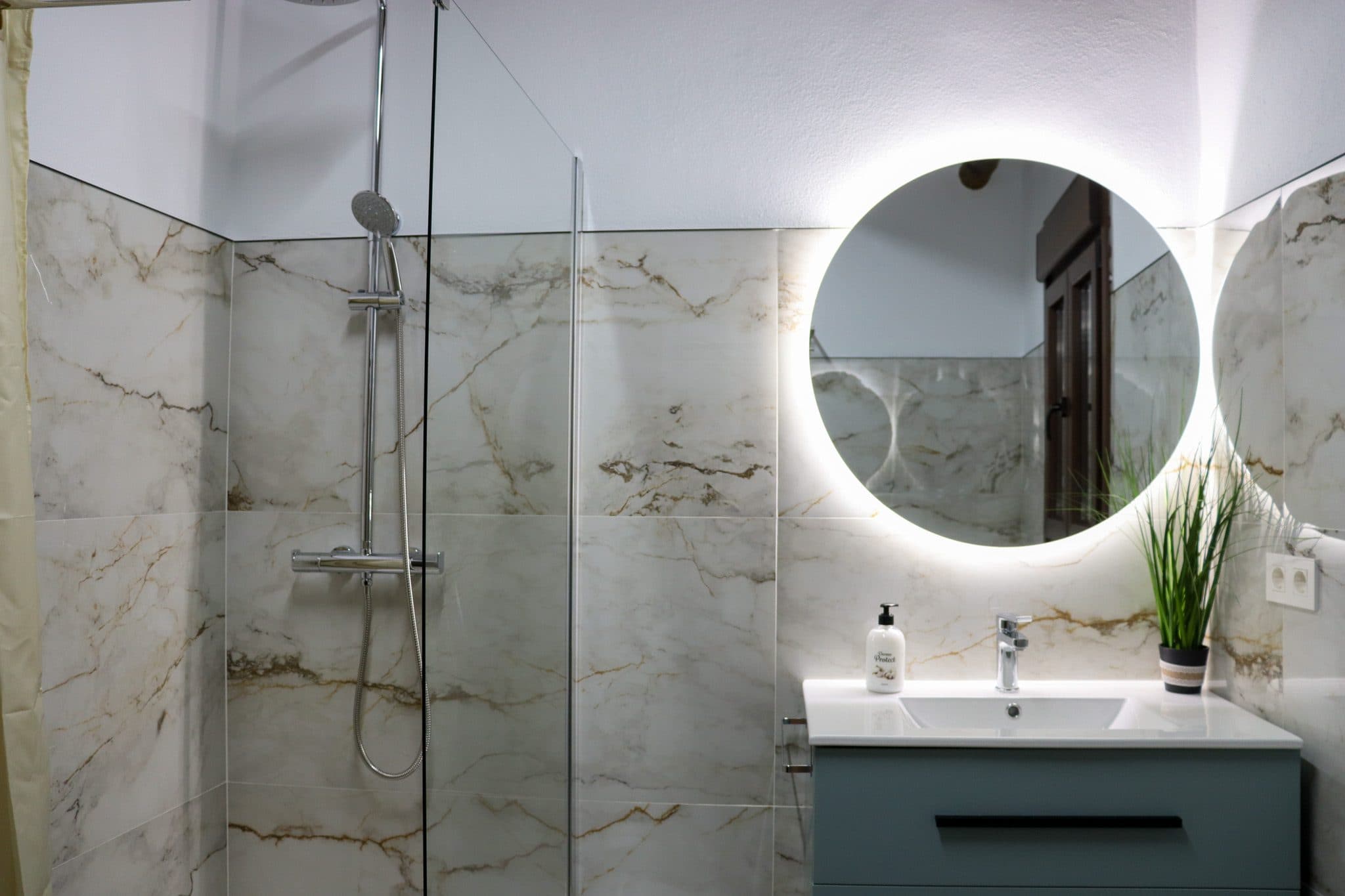 Baño de mármol con ducha de obra y espejo redondo retroiluminado, en la Casa Museo del Trovo y Aguardiente de Murtas