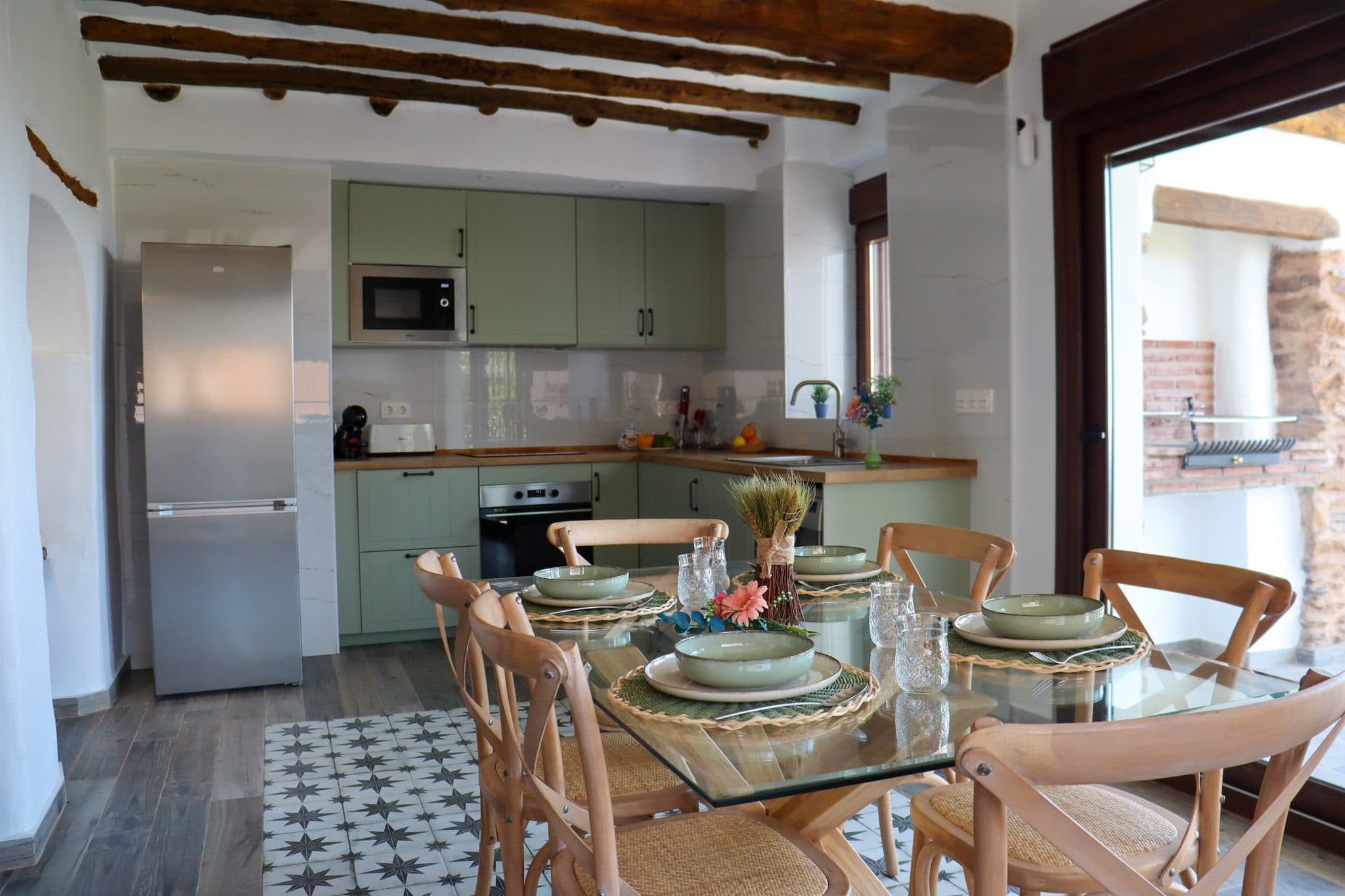 Cocina en verde salvia abierta al comedor, bajo vigas de madera y sobre suelo hidráulico, en la Casa Museo del Trovo y Aguardiente de Murtas