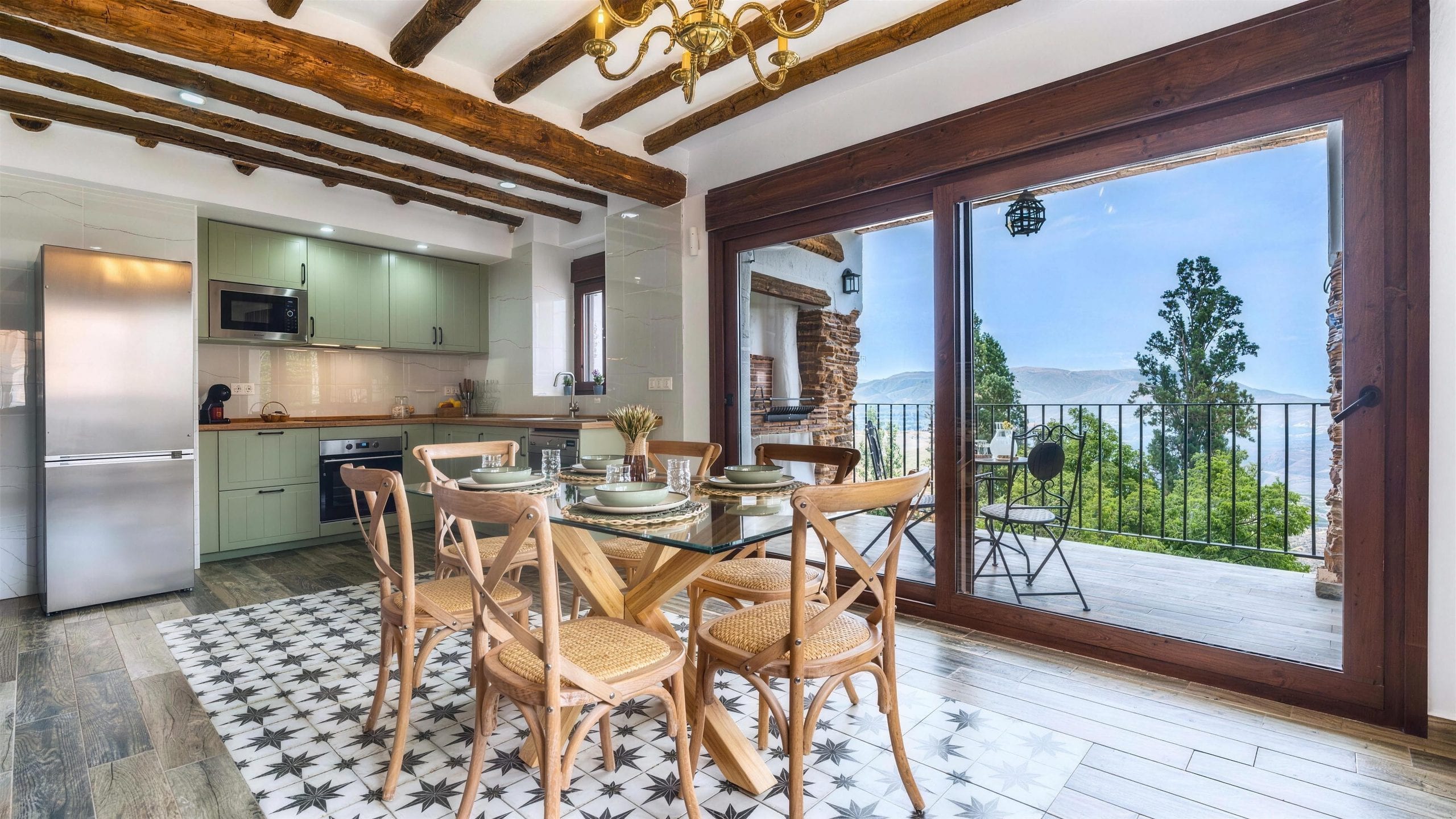 Cocina en verde salvia abierta al comedor bajo las vigas de madera, con el ventanal de par en par hacia la terraza y el valle, en la Casa Museo del Trovo y Aguardiente de Murtas